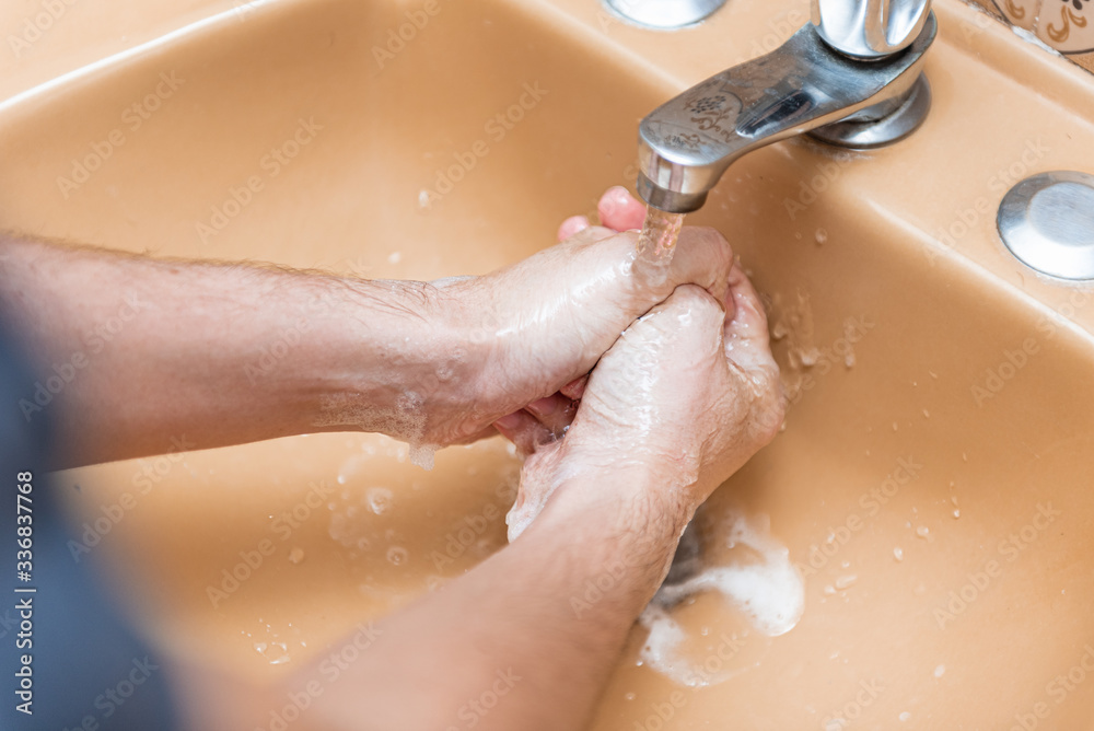 Woman washing hands with soap and water in a yellow sink at home to prevent COVID-19 spread