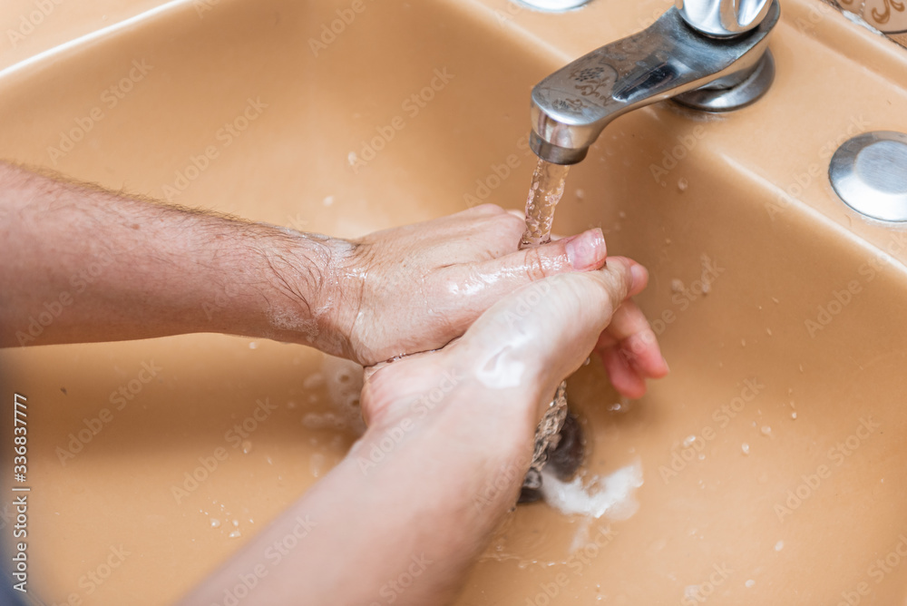 Fototapeta premium Woman washing hands with soap and water in a yellow sink at home to prevent COVID-19 spread