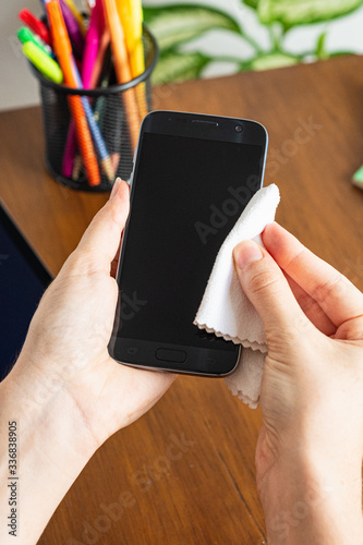 Woman's hand cleaning a smartphone with a white tissue in a home office ambient