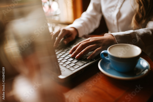 Close up of  a young girl typing on a keyboard lap top next to a cup of coffee