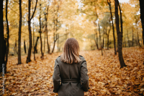 woman in a gray coat is walking along an autumn path in yellow trees and leaves.
