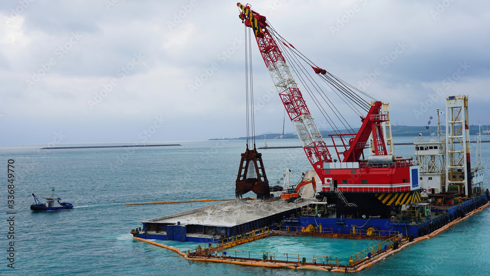 floating crane platform with a huge bucket extracts sand from the bottom of the Pacific Ocean.
a huge crane extracts white sand from the ocean off the coast of Okinawa.