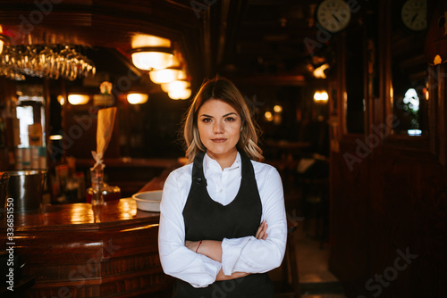 Portrait of young attractive caucasian blonde waitress at cafe entrance