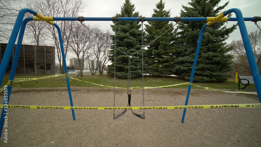 Fototapeta premium Swing set abandoned and locked due COVID-19 coronavirus alert closure, all parks amenities, including, playgrounds, are closed. Yellow caution tape wrapped.