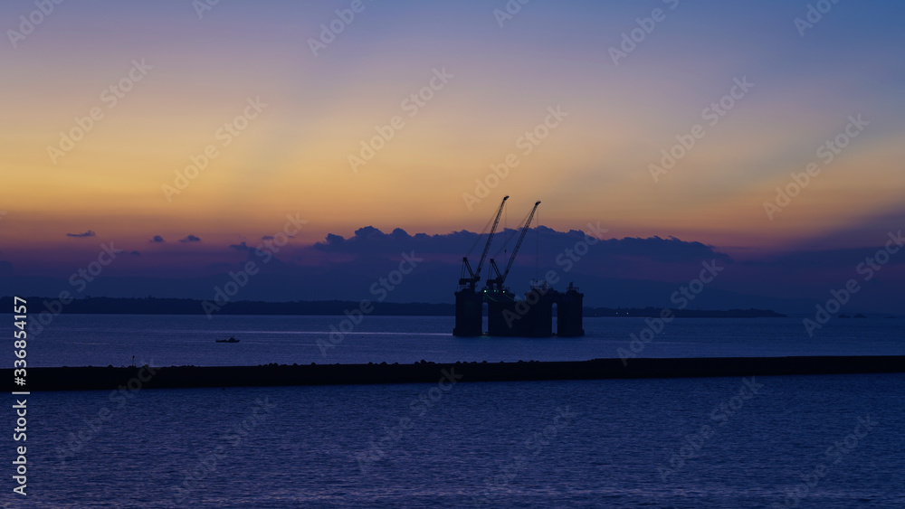floating crane platform in the rays of the setting sun. beautiful golden sunset. industrial cranes in the ocean on a multi-colored sky background. ecology and industry problem