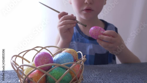 Little blond kid boy coloring eggs for Easter holiday in bath room, indoors. Child holding basket with painted eggs. Child having fun and celebrating feast with easter toy bynny photo