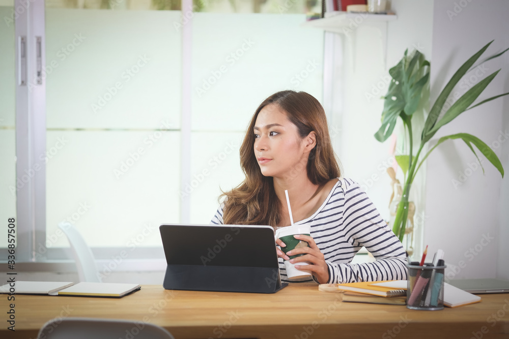 Woman working from home on laptop computer while sitting at the living room, drinking coffee Woman working from home on laptop computer while sitting at the living room, drinking coffee