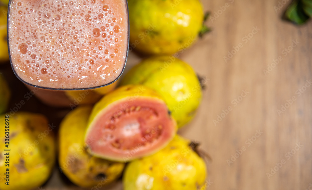 Glass of guava juice (Psidium guajava L.) between leaves and fruits on a neutral background