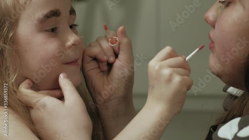 Cheerful child with sister in dresses make each other make-up.