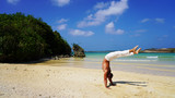 muscular acrobat in white pants on the ocean posing standing on his hands in the trough. mexican hand stand on a sunny day on a tropical beach, back band pose