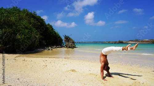 muscular acrobat in white pants on the ocean posing standing on his hands in the trough. mexican hand stand on a sunny day on a tropical beach, back band pose