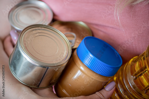 Stock of canned food, butter, peanut butter. Girl holds canned products, peanut butter and olive oil 