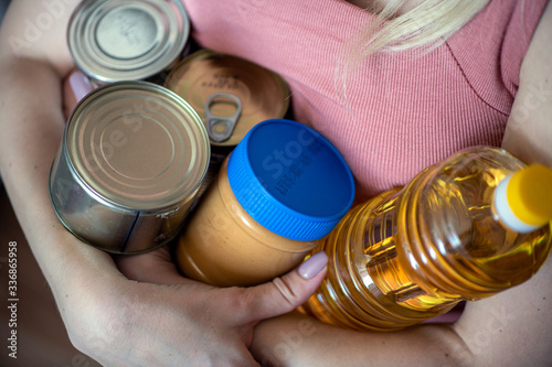 Stock of canned food, butter, peanut butter. Girl holds canned products, peanut butter and olive oil 