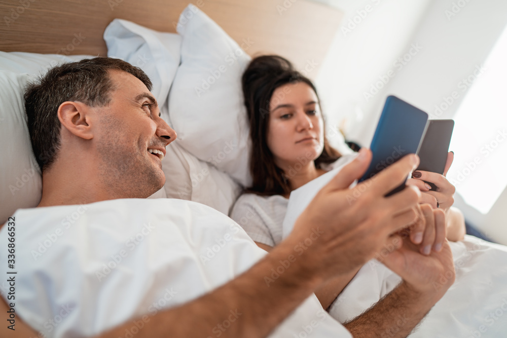Couple laying in the bed and using smartphone Couple laying in the bed and using smartphone