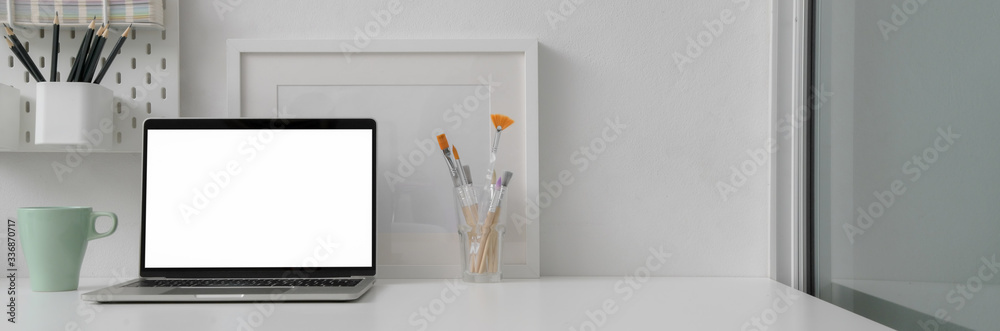 Close up view of artist office desk with blank screen laptop, mug, painting tools and copy space Close up view of artist office desk with blank screen laptop, mug, painting tools and copy space