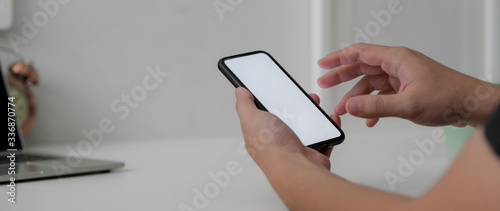 Cropped shot of male freelancer working on blank screen smartphone at minimal home office