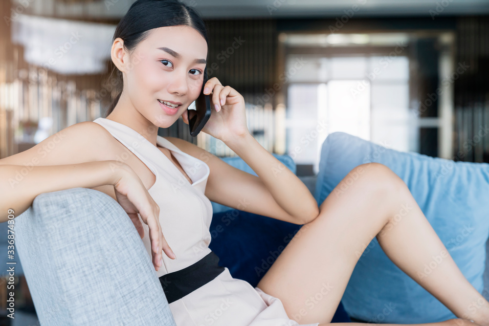 smart attractive beautiful asian female working form home hand use smartphone sit in sosfa couch home interior background relax and casual working expression feeling