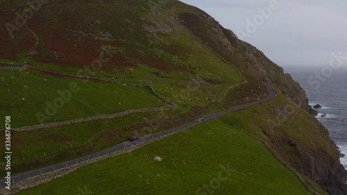 4k aerial video of a car driving on a green mountain road by the oceanside