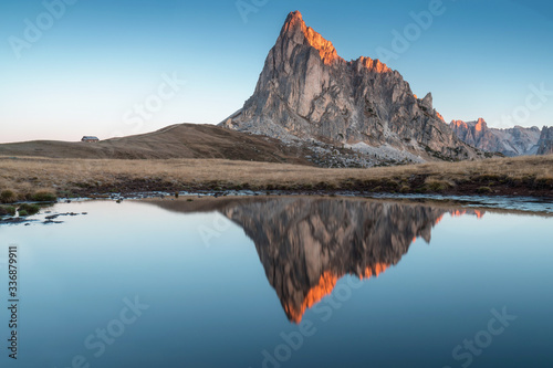 View of famous Dolomites mountain peaks glowing in beautiful golden morning light at sunrise in summer, South Tyrol,Italy Ra Gusella and Giau pass reflection in lake. Famous best alpine place in Alps.