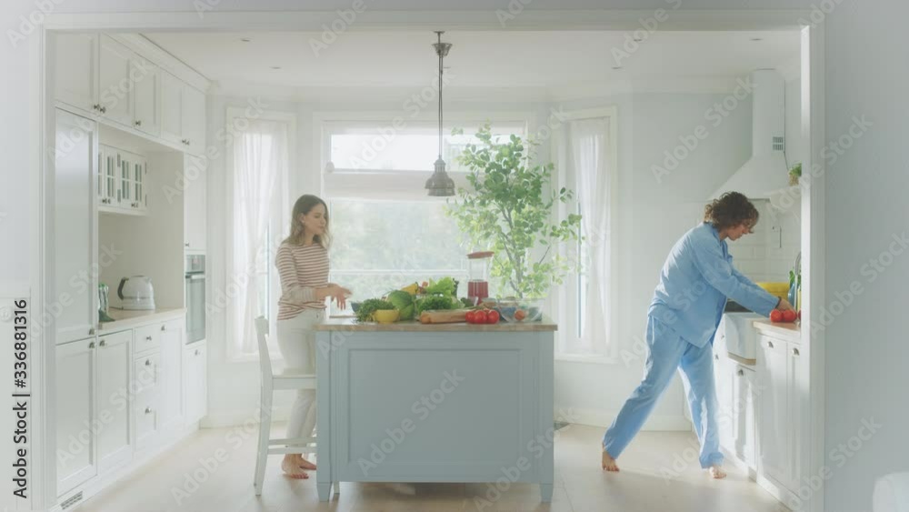 Handsome Young Man in Blue Pajamas and Beautiful Girl are Dancing in the Kitchen. Happy Couple are Juggling Green Vegetable to Each Other. Male and Female at Home on a Sunny Day. Handsome Young Man in Blue Pajamas and Beautiful Girl are Dancing in the Kitchen. Happy Couple are Juggling Green Vegetable to Each Other. Male and Female at Home on a Sunny Day.