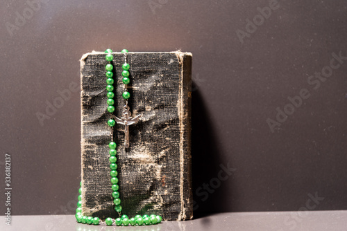 Old religious book with rosary and green crucifix on top on dark background