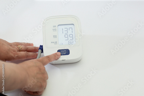 View of cropped hand pressing the blood pressure monitor on white background 