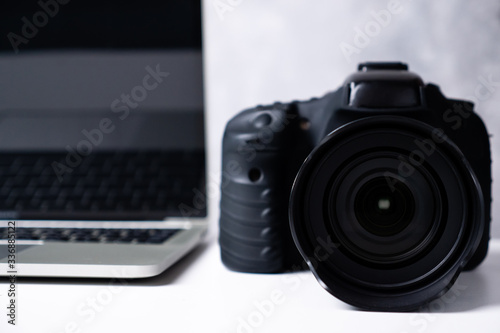 A black digital camera and a computer laptop on a table.