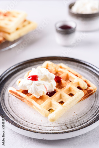 Homemade Belgian Waffles served with whipped cream (Chantilly) and berry jam on grey concrete background. Breakfast. Selective focus