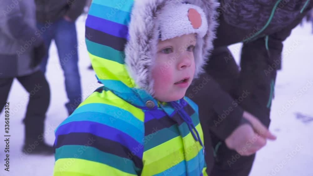 Portrait kid looking at camera with curious face, Active Child boy wearing woolen hat and scarf. Many people behind. Winter St. Petersburg