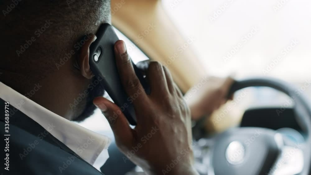 Back view of african man talking phone at car. Man sitting behind steering wheel