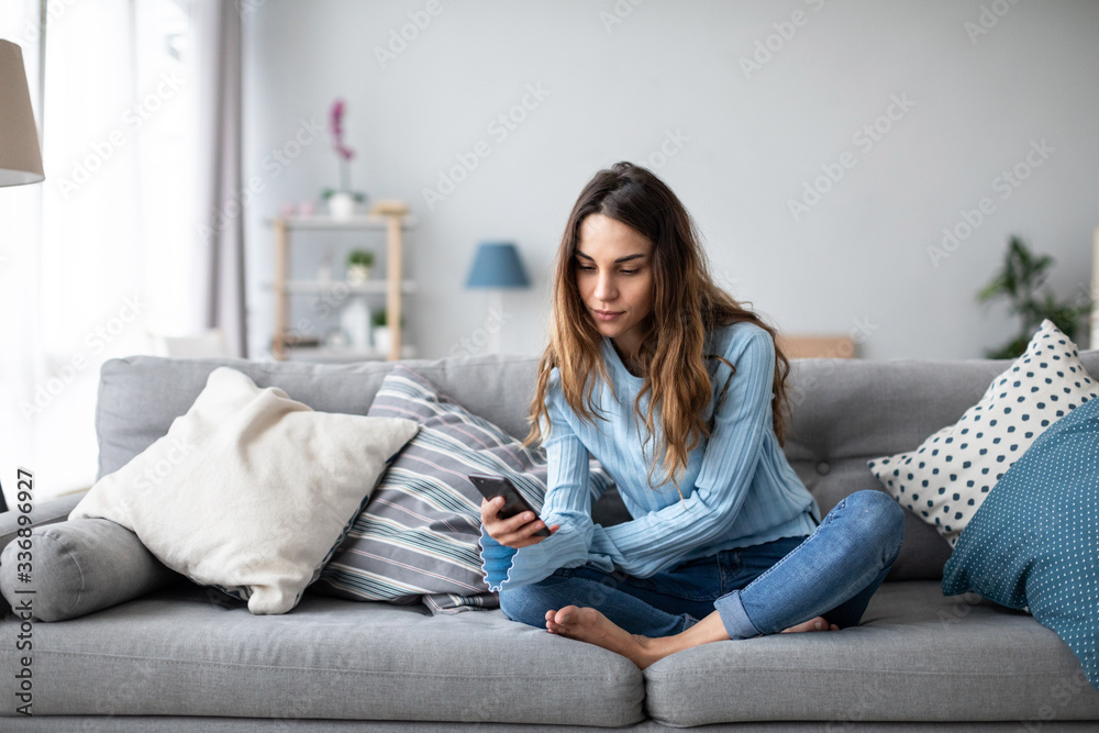 Smiling woman relax sit on sofa at home hold cellphone. Online shoping.