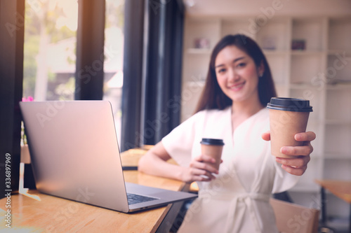 Young woman smile and hold cup of coffee while working with laptop in quarantine.