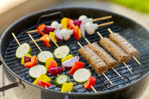 cooking, barbecue and food concept - close up of shish kebab meat and vegetables on bamboo skewers roasting to hot brazier grill outdoors
