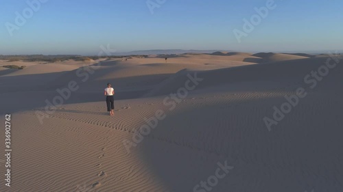 Low aerial 4k cinematic shot of girl taking photos of dogs playing on sand dunes 