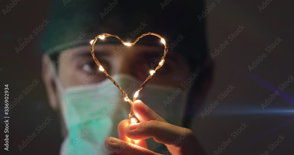 Occhi in primo piano di un medico in prima linea alla lotta al Coronavirus tiene in mano un piccolo simbolo del cuore luminoso per dare speranza alla fine della pandemia Coroanvirus.