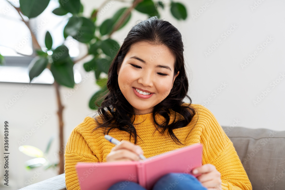 people and leisure concept - happy smiling asian young woman in yellow sweater with diary or notebook sitting on sofa at home people and leisure concept - happy smiling asian young woman in yellow sweater with diary or notebook sitting on sofa at home