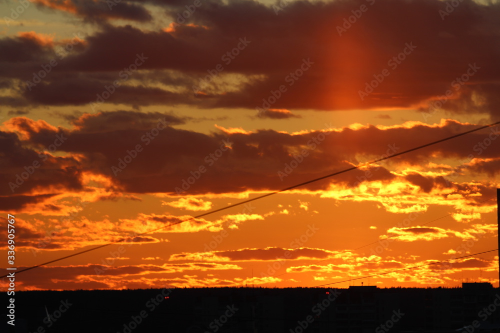 Sun below the horizon and clouds in the fiery dramatic orange sky at sunset or dawn backlit by the sun. Place for text and design. Sun below the horizon and clouds in the fiery dramatic orange sky at sunset or dawn backlit by the sun. Place for text and design.