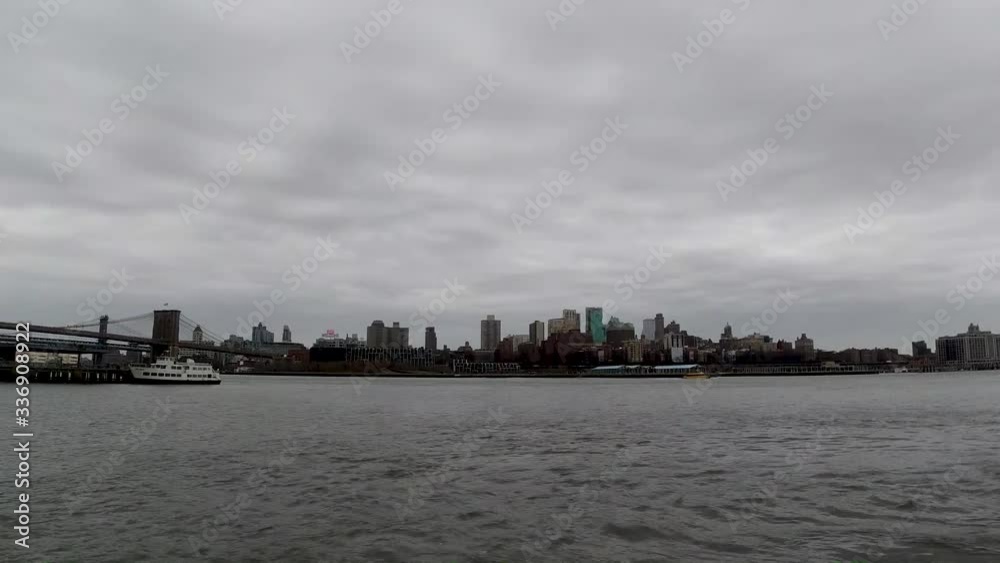 A timelapse over East River of Brooklyn industrial skyline from Manhattan as boats pass by on a cloudy day A timelapse over East River of Brooklyn industrial skyline from Manhattan as boats pass by on a cloudy day