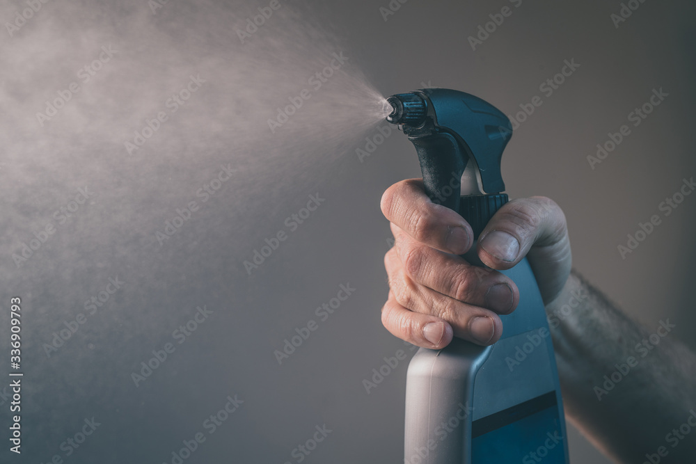 A person holding a spray bottle with disinfection liquid and spraying.  Visible drops of spray in attempt to destroy covid or corona virus  threatening our lives. Stock Photo | Adobe Stock