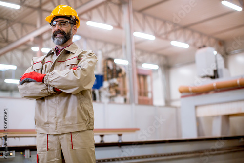 Confident mature man standing with crossed arms in the factory manufacturing unit with orange helmet
