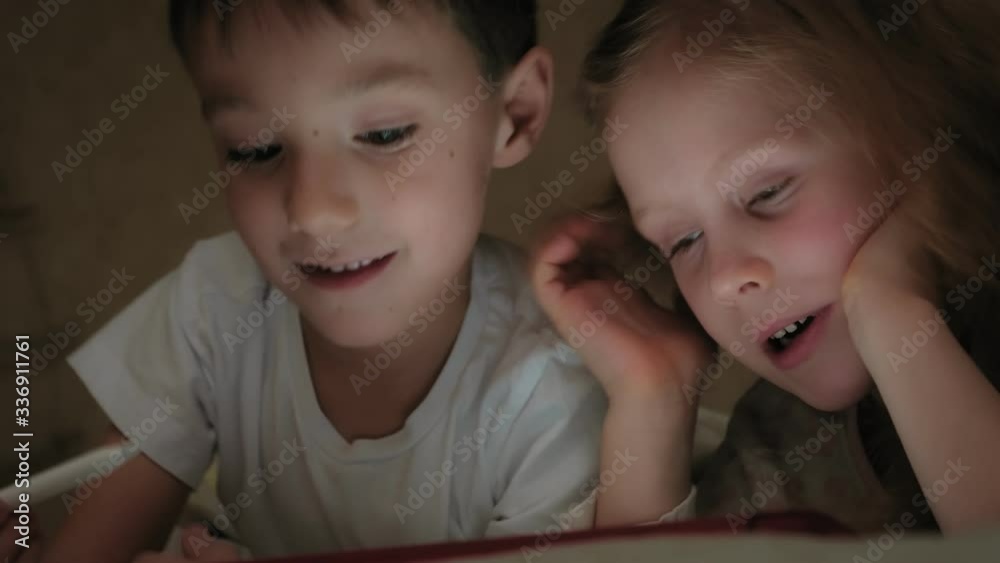 Little children, brother and sister are lying on the bed and playing on the tablet before going to bed. Little children, brother and sister are lying on the bed and playing on the tablet before going to bed.