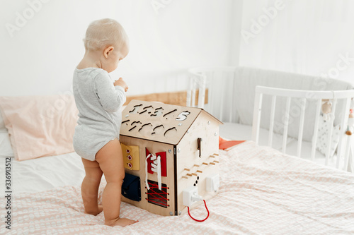 Montesori and the bizibord. A small child plays with a wooden house in the room on the bed, developing his motor skills.