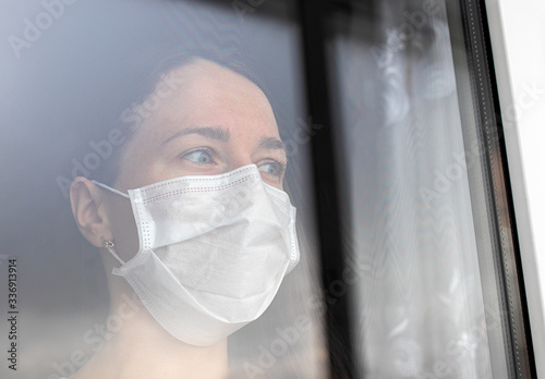the girl in the medical mask looks anxiously out the window. isolation, quarantine