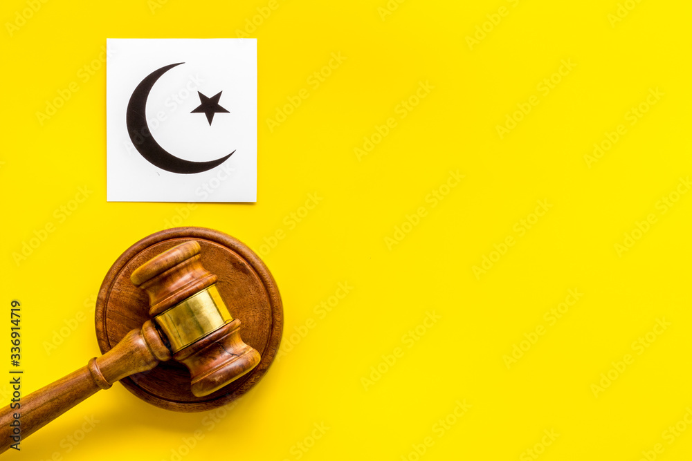 Islam sybmbol crescent and star near gavel on yellow table top view. Religious conflict concept. Copy space