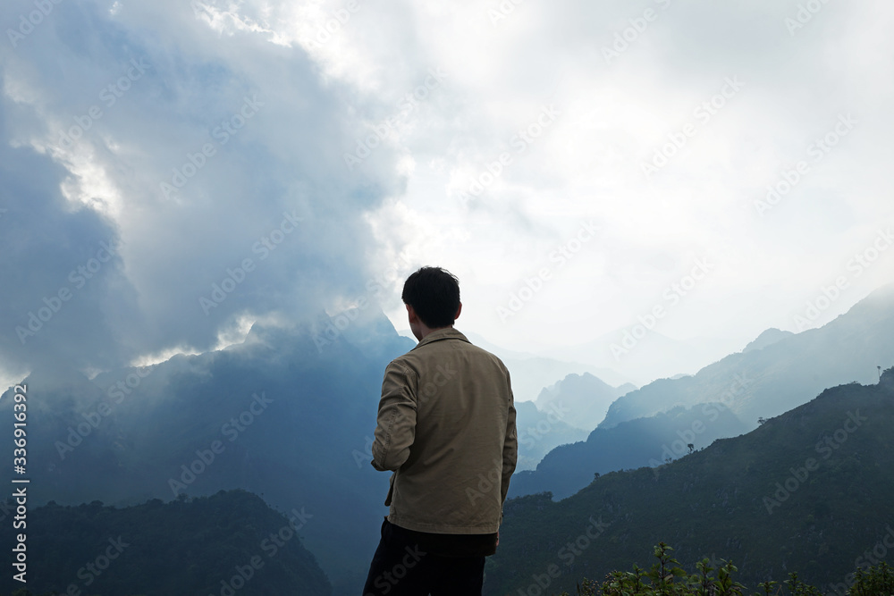 Fototapeta premium A man standing on the peak looking at green mountain range with cloudy sky
