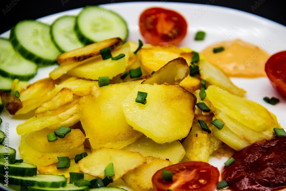 Homemade fried potatoes with fresh cucumbers, cherry tomatoes and sauces on the white plate. Delicious ukrainian fried potatoes with vegetables against background. Cooked tasty meal for lunch.