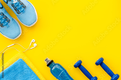 Athletics background with dumbbells, towel, sneakers on yellow background top view copy space