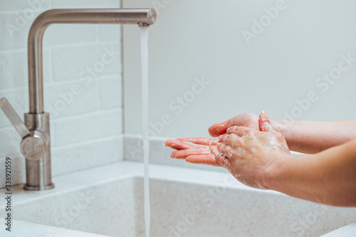 Close-up of woman washing hands with soap in the bathroom.