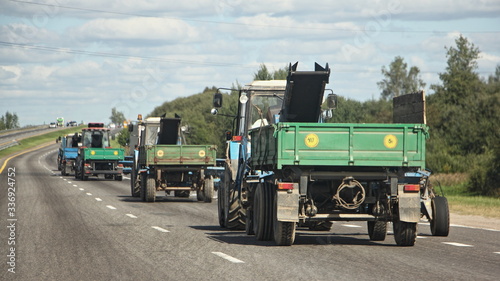 Tableau sur toile A many tractors convoy with flatbed trailers rides on a suburban road on a Sunny