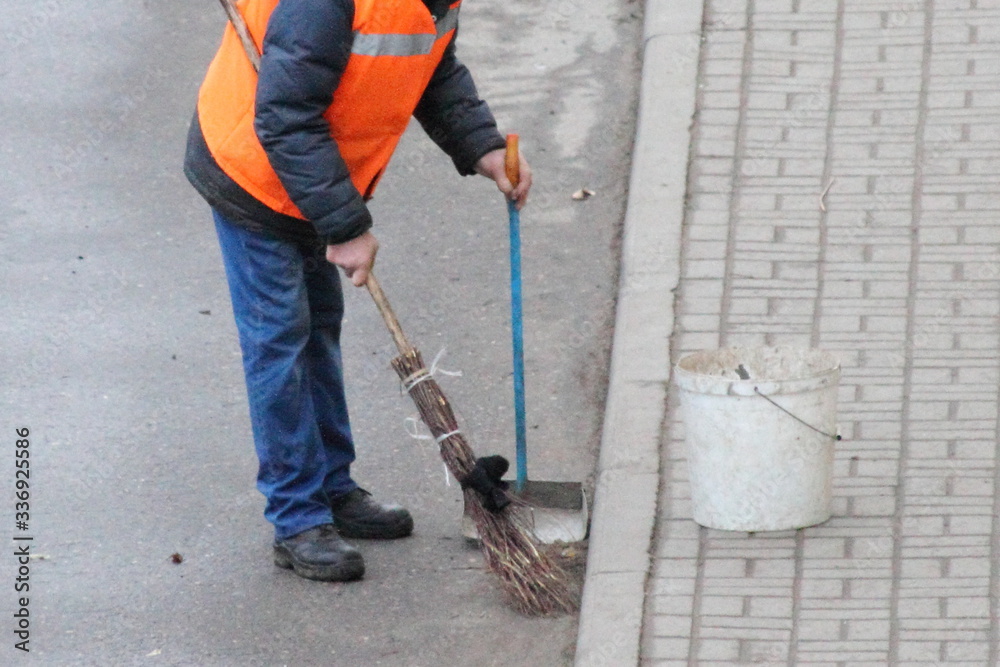 Close up janitor men in an orange uniform jacket sweeps the paved street road with a broom, top side view Close up janitor men in an orange uniform jacket sweeps the paved street road with a broom, top side view